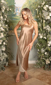 Woman in a beige satin dress standing in a decorated room with flowers and a painting.