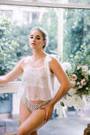 Woman in lace lingerie standing outdoors with flowers and greenery in the background