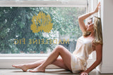 Woman in a white dress sitting by a window with 'Madeleine Fig' logo.