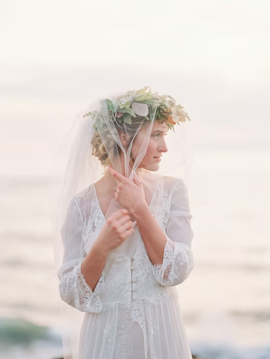 Woman in a white lace dress with a floral headpiece against a blurred natural background