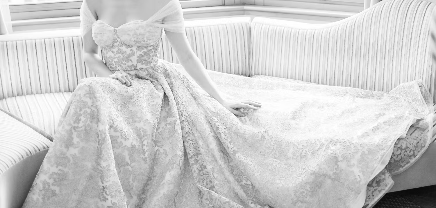 Woman in a white lace wedding dress sitting on a white couch.