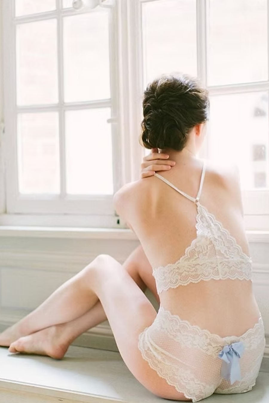 Woman in lace lingerie sitting by a window with soft natural light.