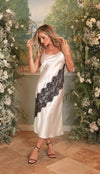 Woman in a white dress with black lace details standing in front of floral decorations.