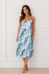 Woman wearing a blue floral dress against a white paneled wall.