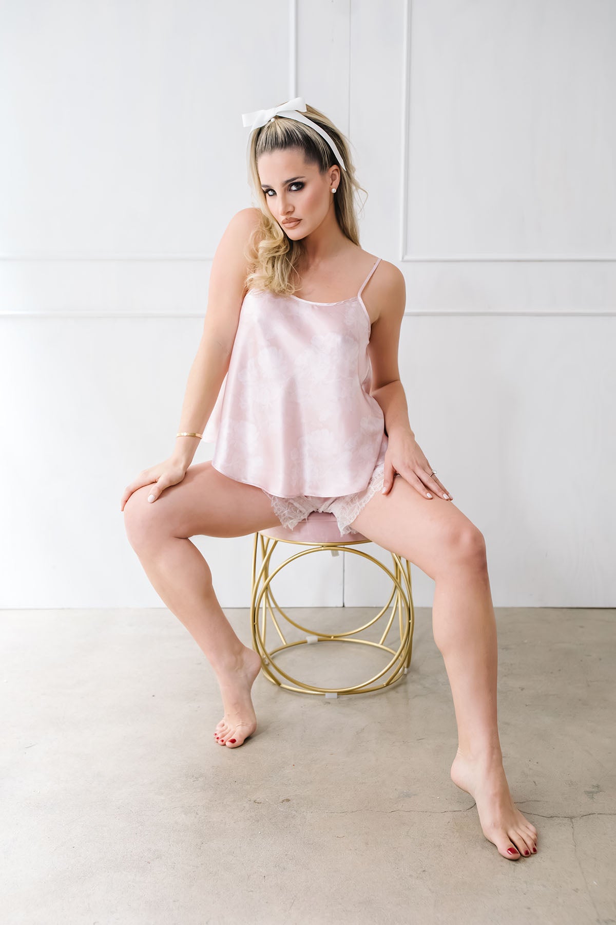 Woman wearing a pink satin slip sitting on a gold stool against a white background