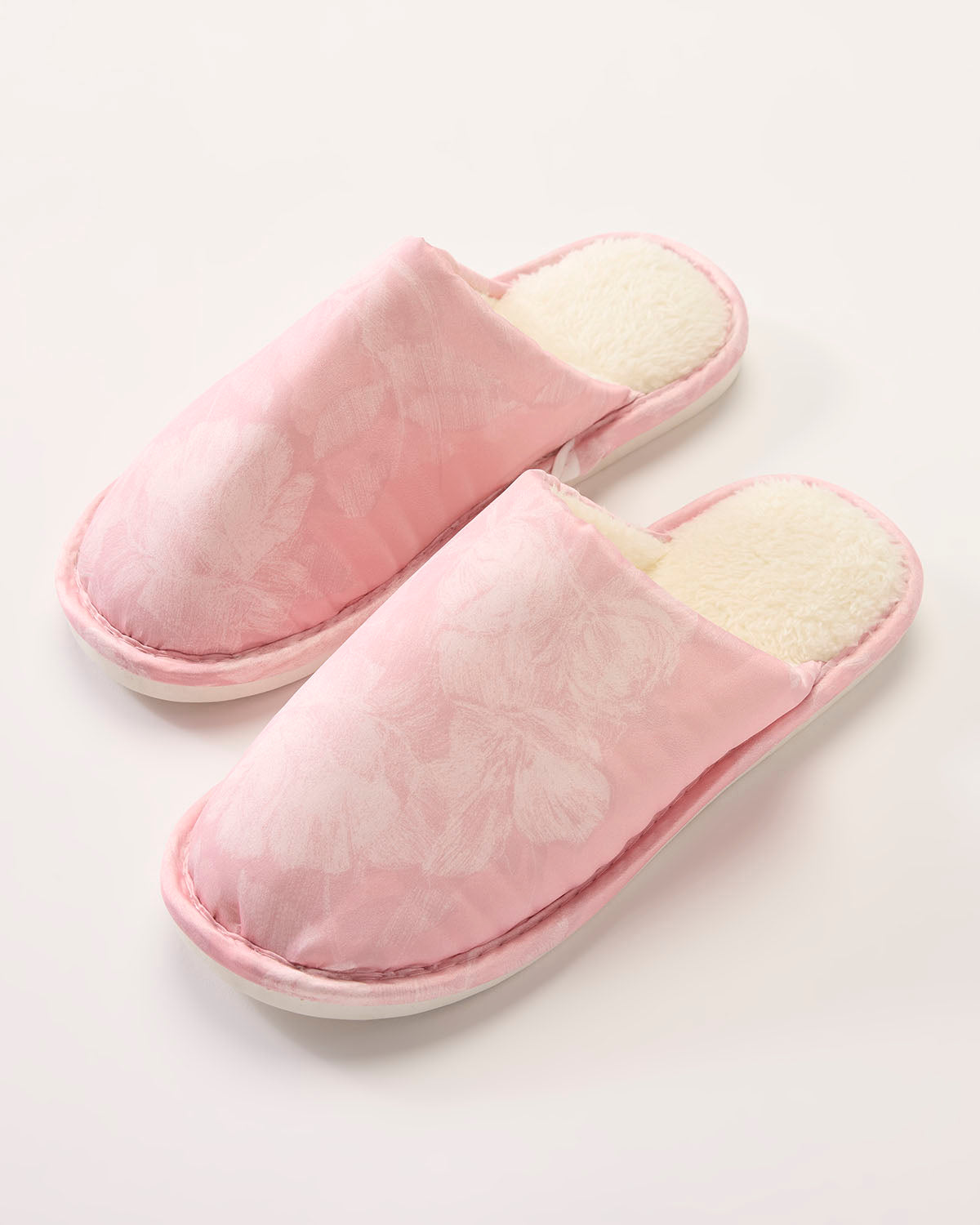 Pair of pink slippers with white interior on a light gray background